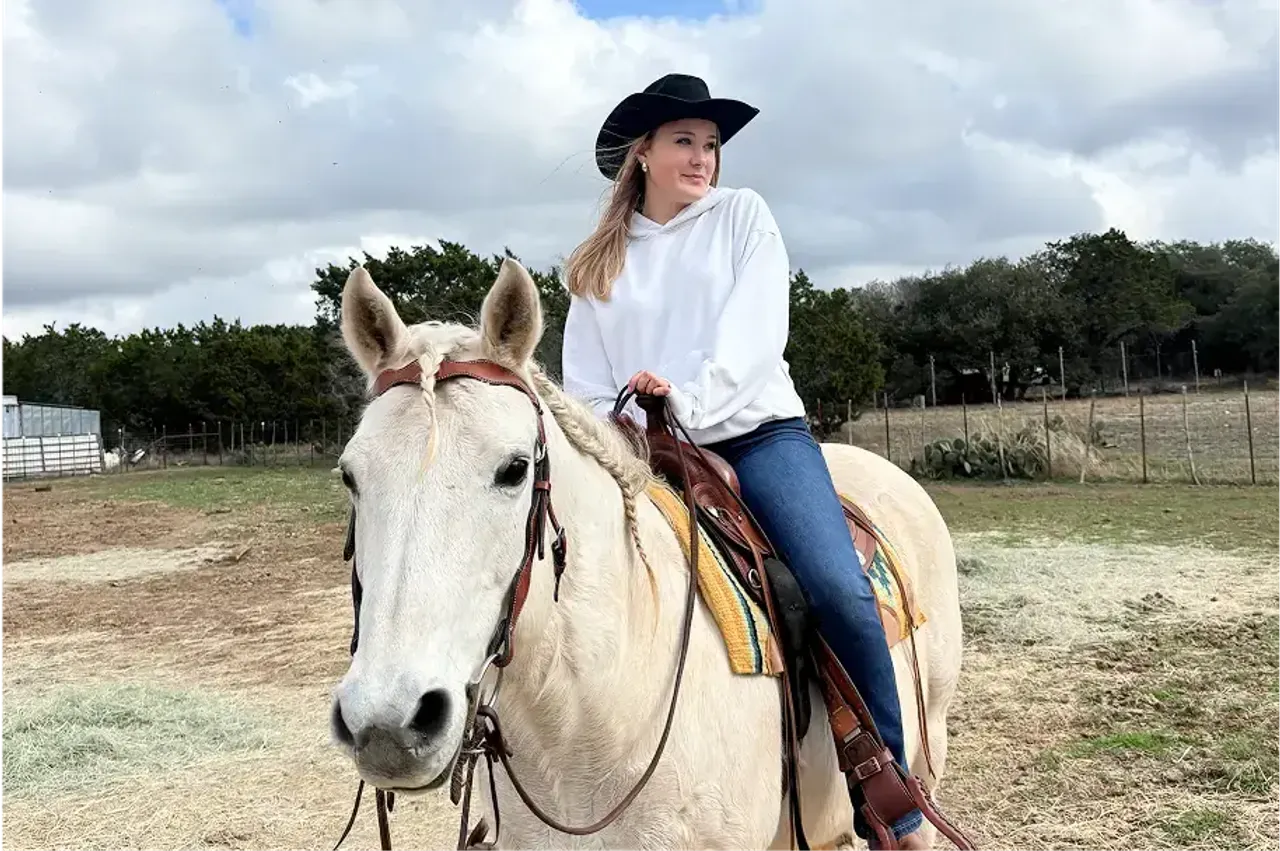 Studentessa con cappello da cowboy in sella a un cavallo bianco in un ranch negli Stati Uniti