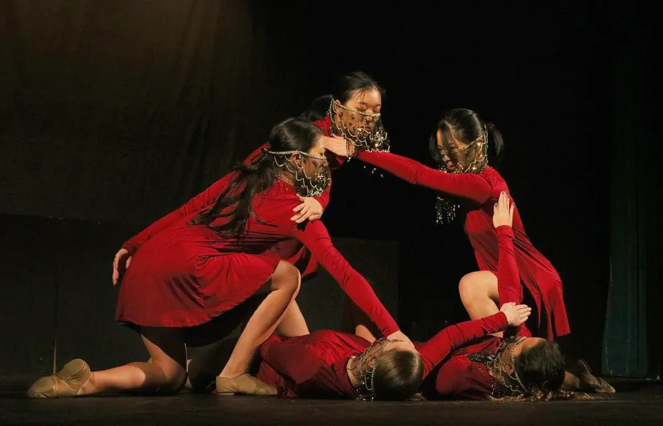 Un gruppo di studenti della Alameda High School esegue sul palco uno spettacolo di danza in costumi rossi.