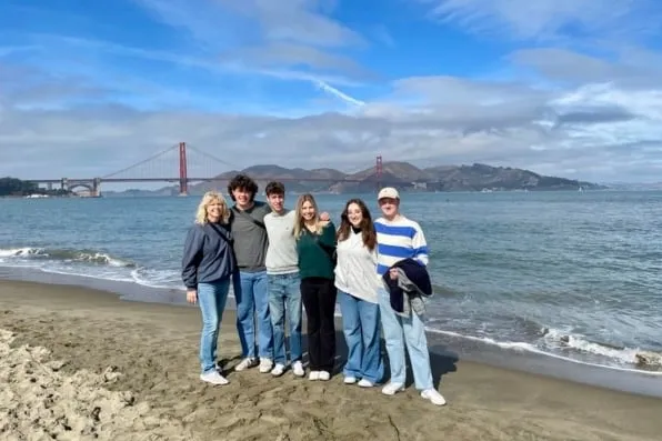 Seis personas posan sonrientes en una playa con el gran puente rojo de fondo