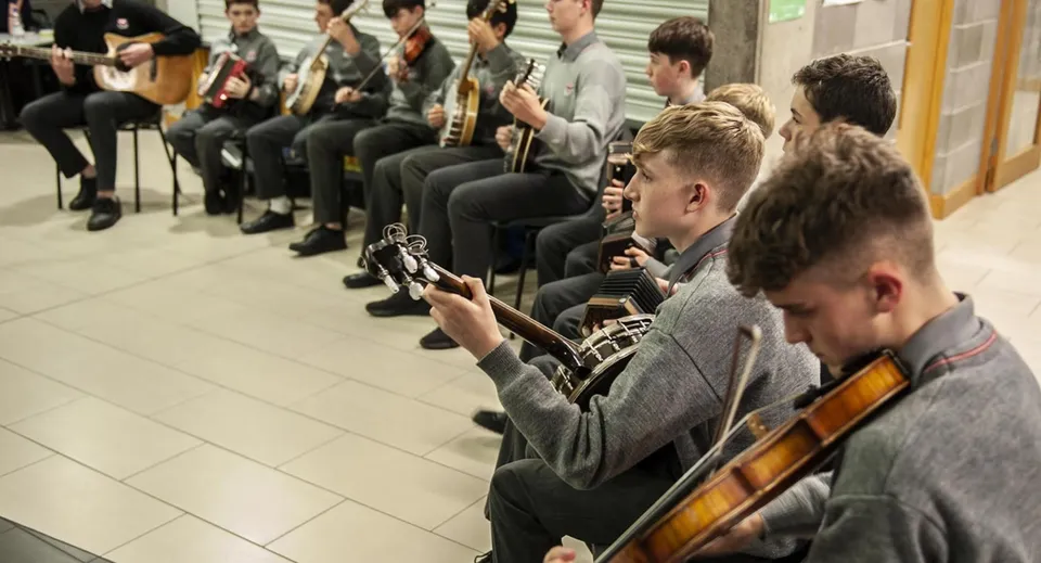 Studenti e studentesse suonano vari strumenti musicali come chitarre e violini durante la lezione di musica al Coláiste Choilm.