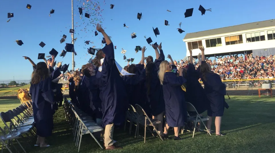 I diplomati della Ovid-Elsie High School lanciano i loro tocchi in aria e festeggiano il diploma sul campo sportivo.