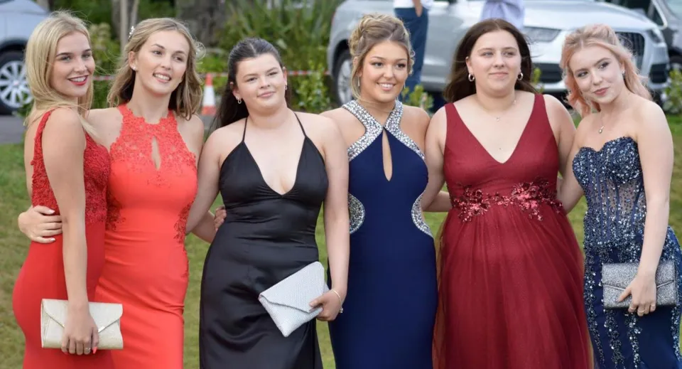 Sei studentesse della Truro High School for Girls posano insieme in eleganti abiti da sera all'aperto su uno sfondo verde.