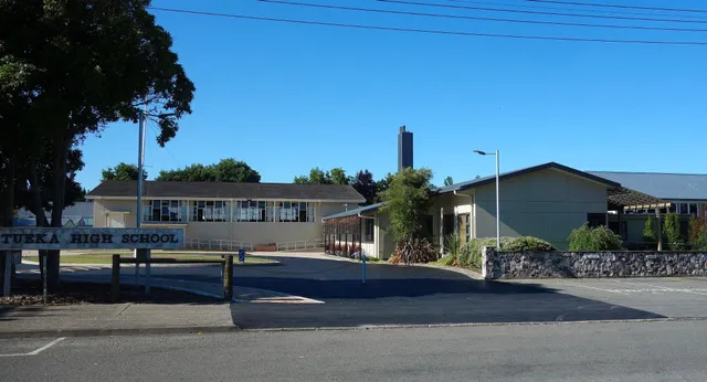 L'edificio scolastico con un'alta torre della Motueka High School si trova sullo sfondo circondato da alberi e da un parcheggio pavimentato.