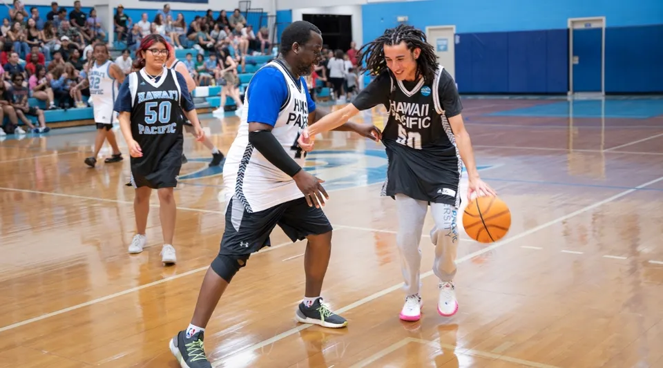 Due giocatori di basket della Hawai'i Pacific University palleggiano sul campo davanti agli spettatori.