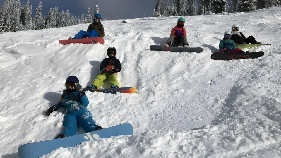 Studenti della École des Sentiers-Alpins scendono con lo snowboard lungo un pendio innevato in un bosco invernale.