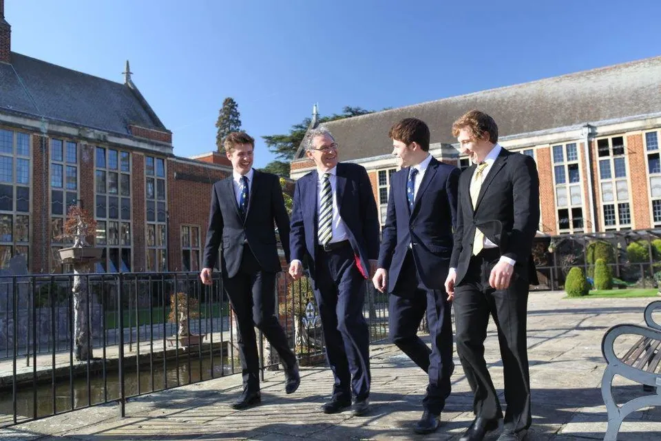 Quattro uomini in abiti formali sono insieme davanti a un edificio del campus della Whitgift School.