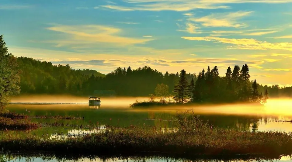 Un lago tranquillo con una piccola barca e circondato dal bosco al tramonto.