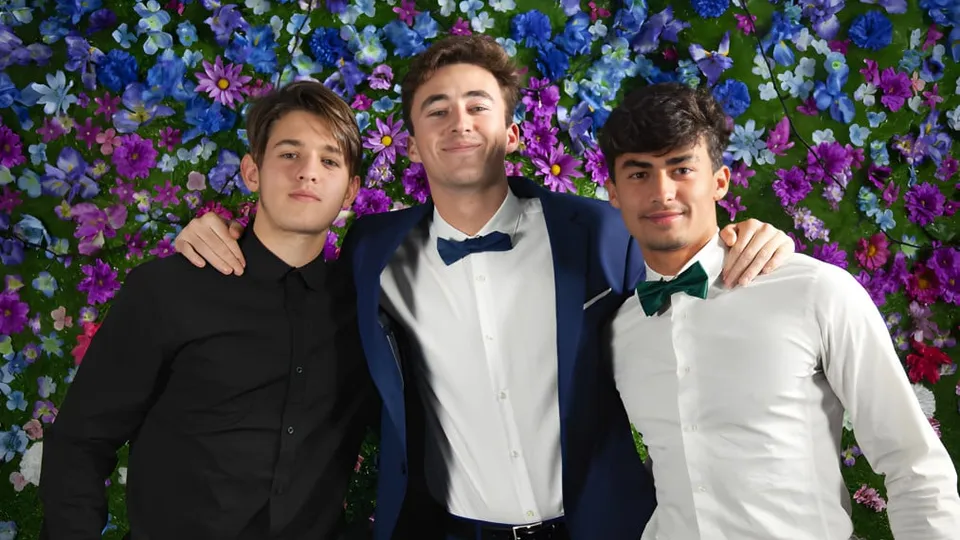 Drei Schüler des F-1 No Choice Programms USA posieren gemeinsam vor einem farbenfrohen Blumenhintergrund.