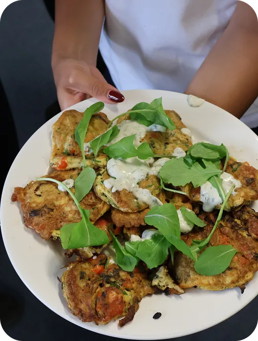Plato de tortitas de verdura con rúcula y salsa de yogur sostenido entre las manos