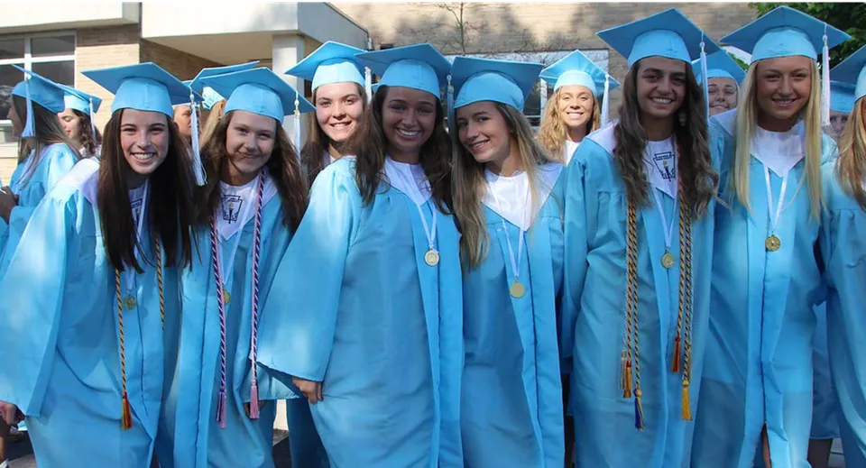 Un gruppo di diplomate e diplomati della Holland Park State High School posa in toga blu davanti a un edificio e festeggia il proprio diploma.