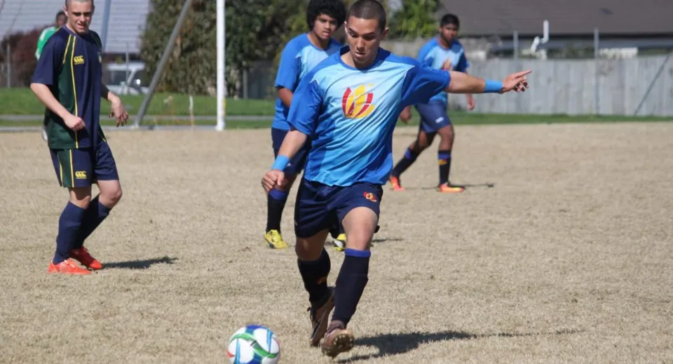 Un gruppo di studenti gioca a calcio sul campo sportivo dell'Alfriston College, mentre un giocatore guida la palla al piede.