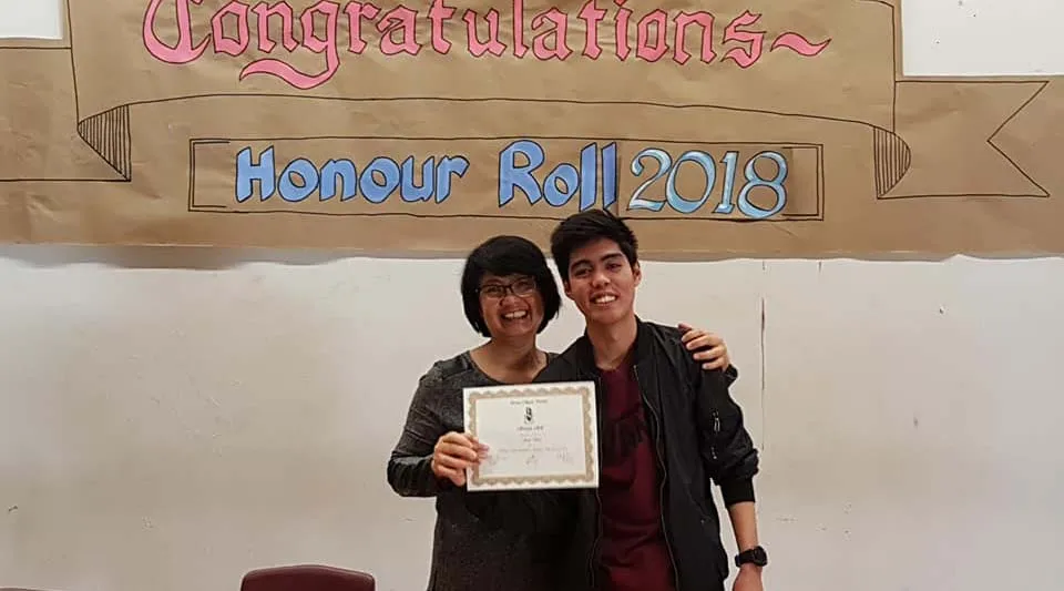 Due persone tengono insieme un certificato davanti a uno striscione nel campus dell'Emery Collegiate Institute.