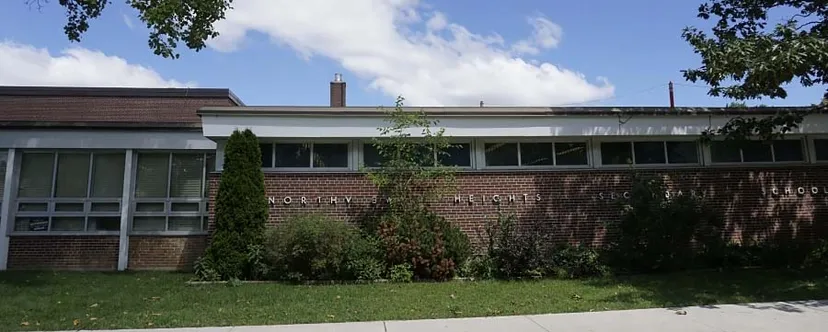 L'edificio in mattoni della Northview Heights Secondary School si trova su un prato davanti ad alberi sotto un cielo parzialmente nuvoloso.