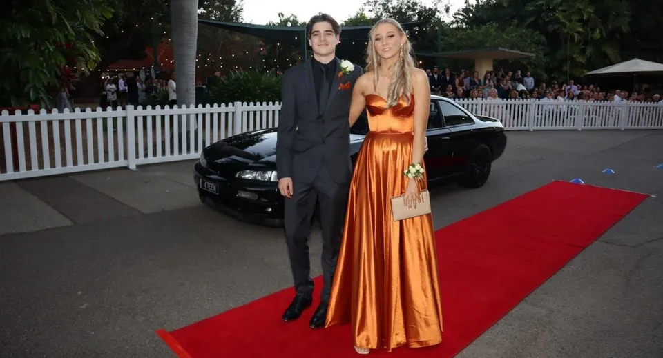 Una studentessa e uno studente della Townsville Grammar School in abito formale sul tappeto rosso davanti a un'auto nera.