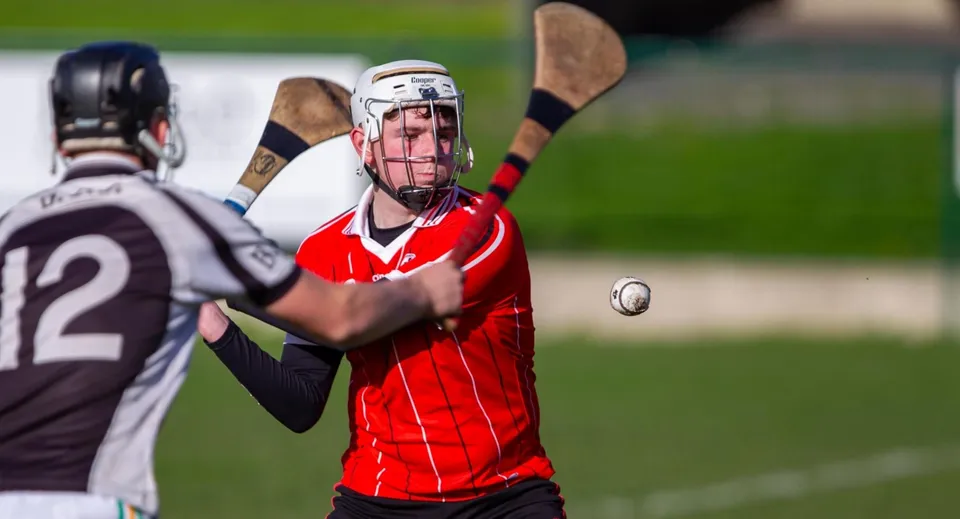 Uno studente della St. Aidan's Comprehensive School gioca a hurling con casco e bastone sul campo sportivo.