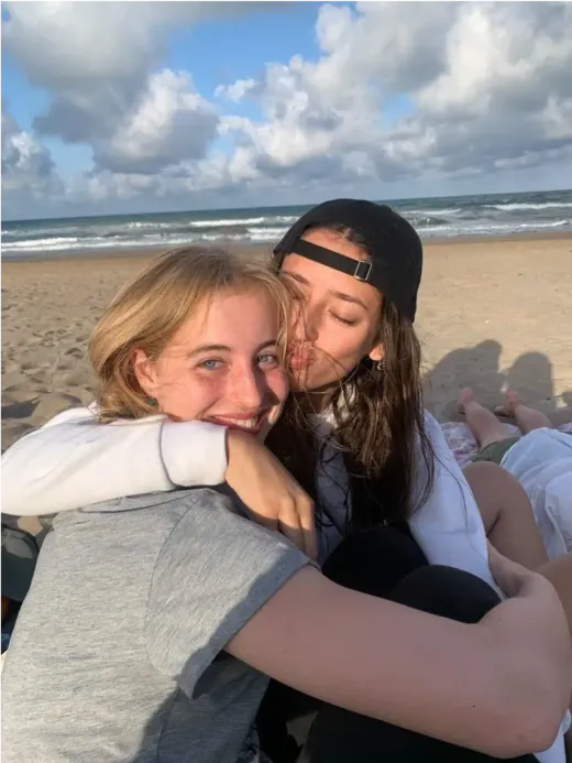 Zwei lächelnde Mädchen umarmen sich für ein Selfie am Strand in Spanien