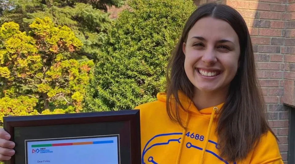 Una studentessa della St. Anne Catholic High School sorride mentre tiene in mano un attestato incorniciato all'aperto.