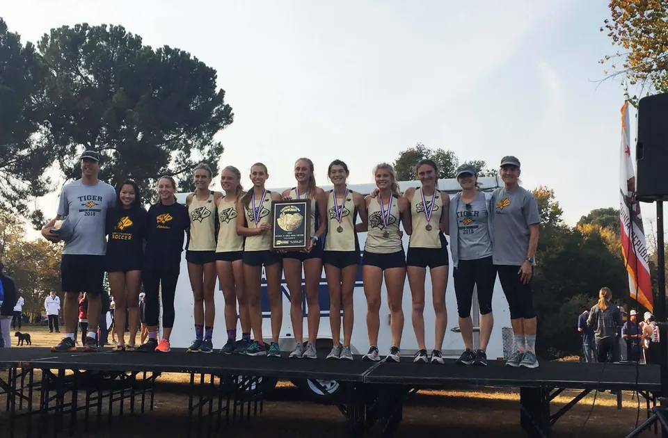 Un gruppo di giovani atlete della San Luis Obispo High School è in piedi con dei trofei su un palco, davanti ad alberi e a un cielo terso.