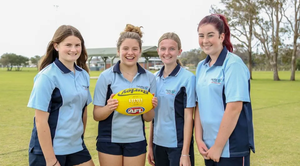 Quattro studentesse del Dalyellup College sono insieme su un campo in erba e tengono in mano un pallone da Australian Rules Football.