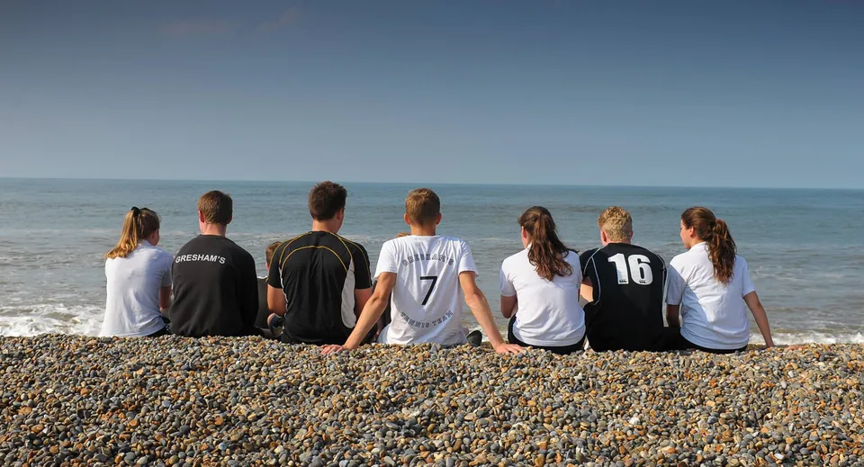 Un gruppo di persone siede su una spiaggia di ciottoli con vista sul mare calmo nella tenuta della Gresham’s School.