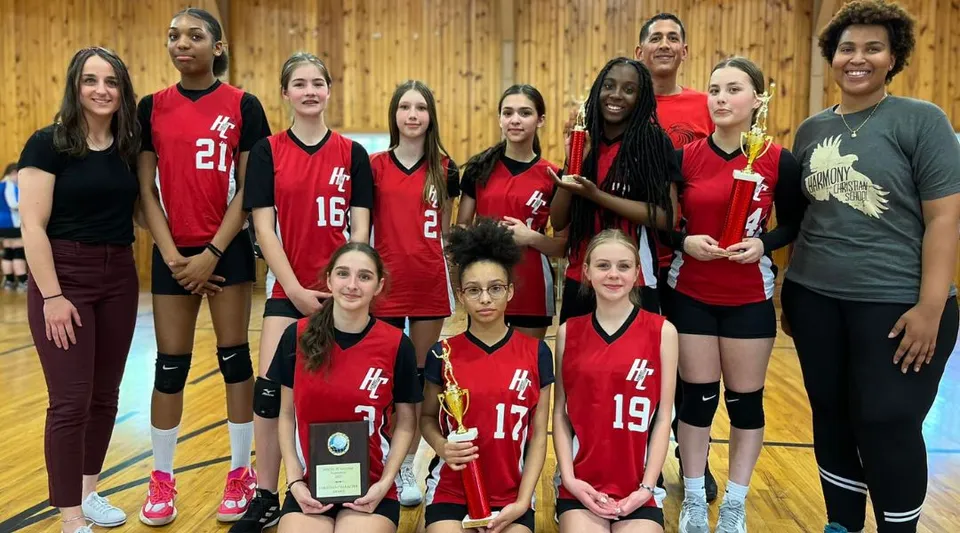 Un gruppo di giovani atlete in maglia rossa posa insieme nella palestra della Harmony Christian School.