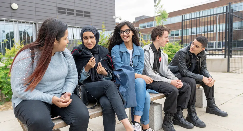 Studenti seduti su una panchina davanti a un edificio dal design moderno nel campus della Langley Secondary School.