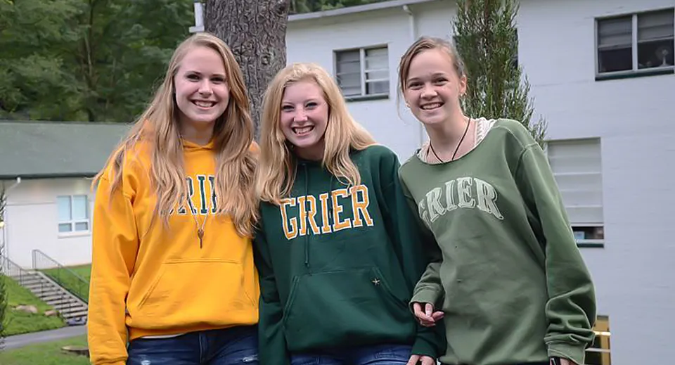 Tre studentesse della Grier School sorridono insieme davanti a un edificio residenziale.