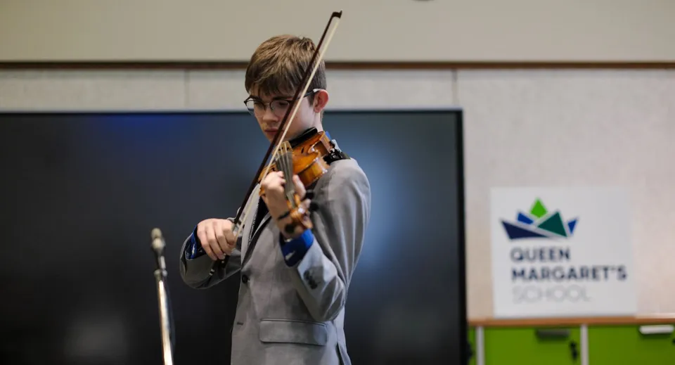 Una studentessa suona il violino davanti a un cartello della Queen Margaret's School.