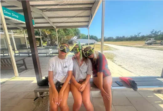 Drei Mädchen mit Schnorchelmasken sitzen auf einer Bank vor einem Tauchshop in Australien