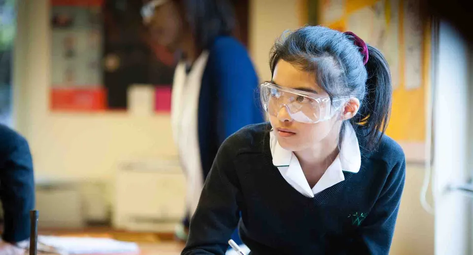 Una giovane donna in completo nero con gli occhiali sta concentrata in una stanza disordinata della Wychwood School.