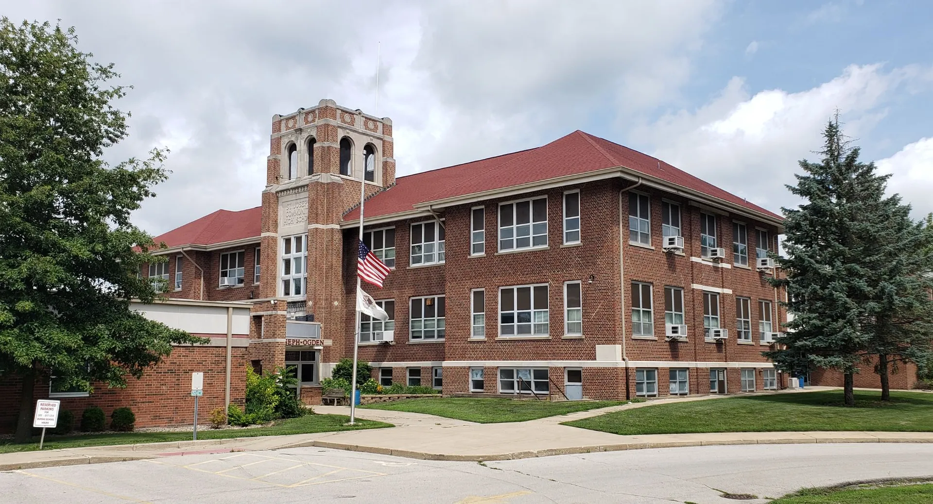 L'edificio in mattoni con un'alta torre dell'orologio nel campus della Quad Cities Christian School, circondato da alberi e da una bandiera americana.