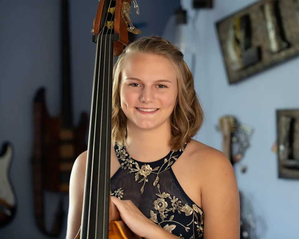 Una studentessa della Queensbury High School tiene in mano un violoncello in una stanza con opere d'arte alle pareti.