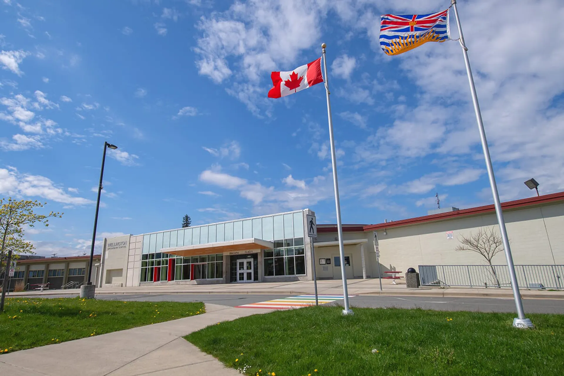La bandiera canadese sventola sopra il moderno edificio in vetro della Wellington Secondary School sotto un cielo blu.