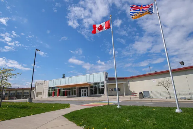 La bandiera canadese sventola sopra il moderno edificio in vetro della Wellington Secondary School sotto un cielo blu.