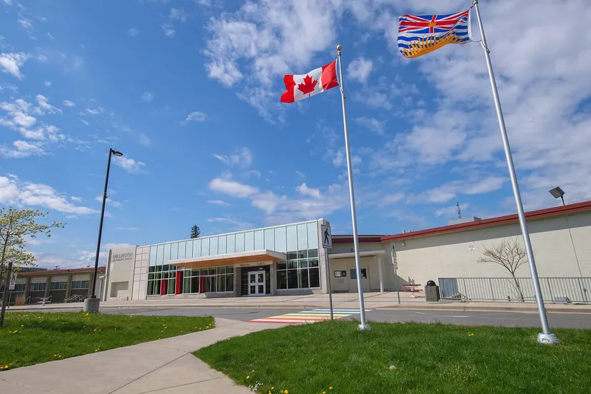 La bandiera canadese sventola sopra il moderno edificio in vetro della Wellington Secondary School sotto un cielo blu.