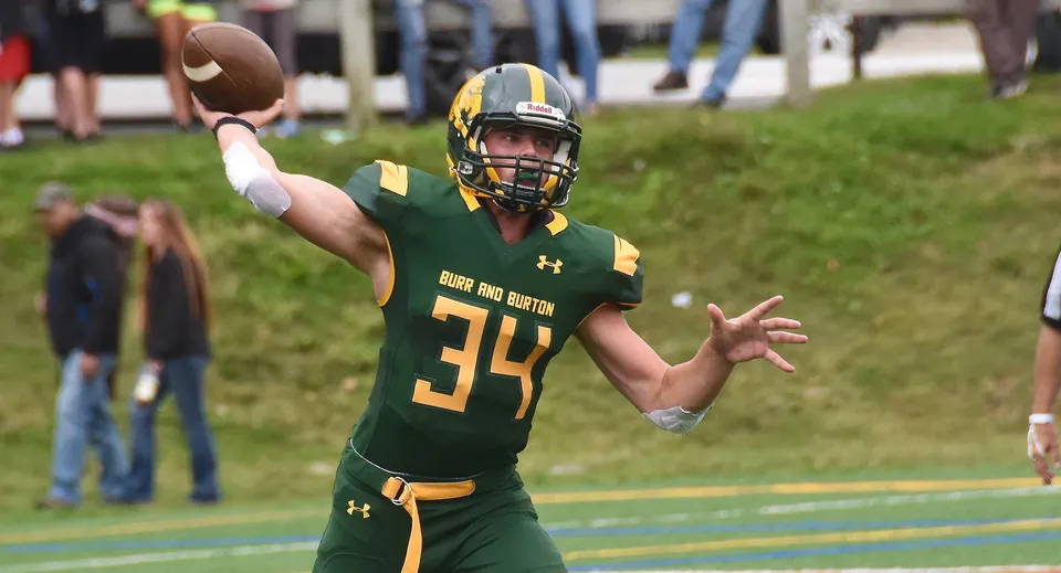 Un giocatore di football della Burr and Burton Academy in maglia verde lancia un pallone da football sul campo.