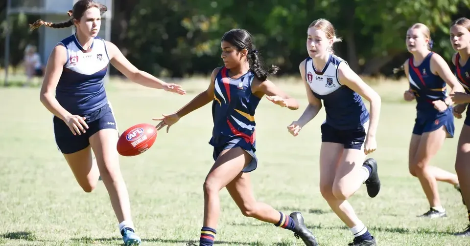 Studentesse della St. Hilda’s School giocano a football australiano su un campo in erba.