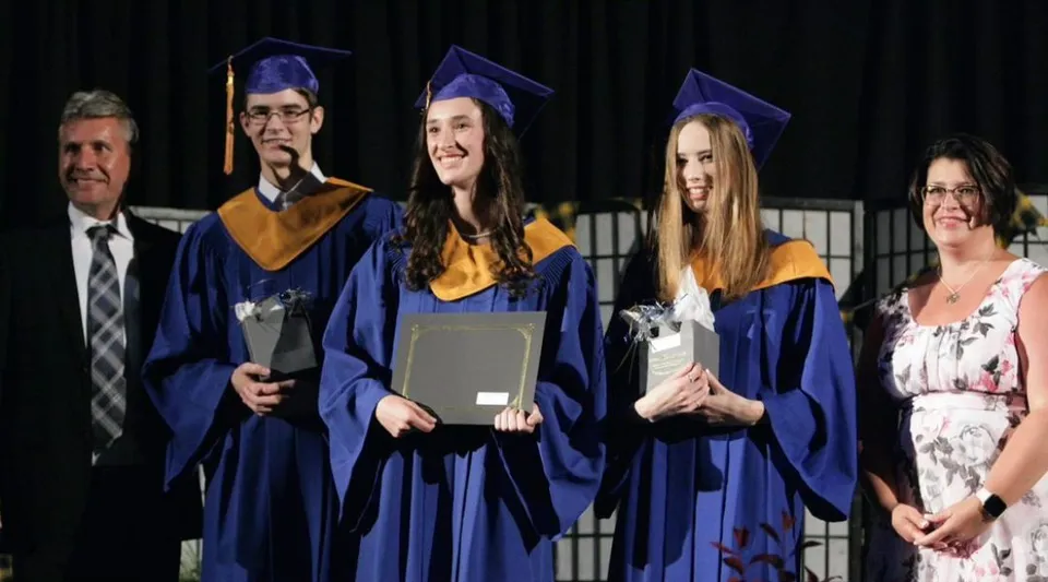 I diplomati della Char-Lan District High School sul palco in toga blu con i docenti sullo sfondo.