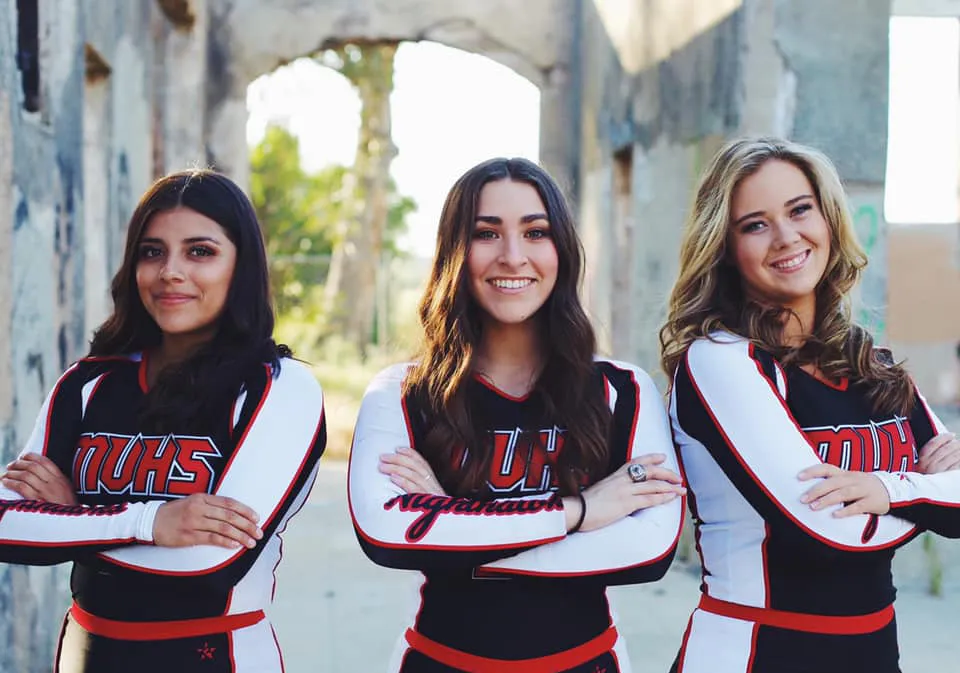 Tre studentesse della Murietta Valley High School si trovano davanti a un muro di mattoni e indossano maglie sportive uguali con la scritta UHS.