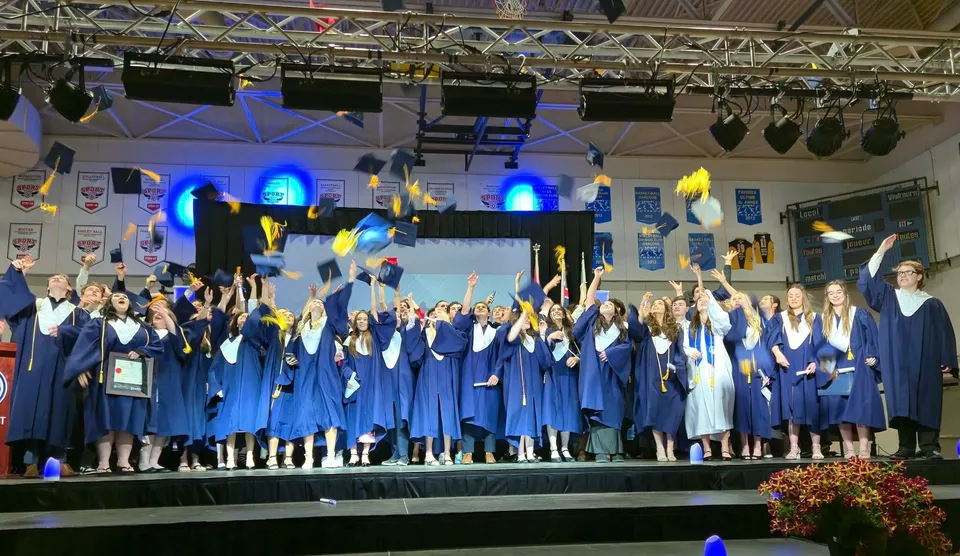 I diplomati della École secondaire publique Le Sommet sono sul palco con le loro toghe blu da diploma e le luci del palcoscenico sullo sfondo.