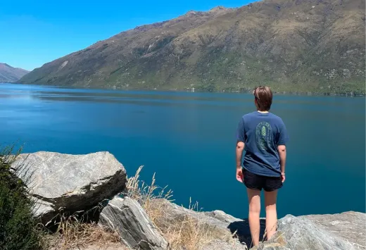 Louisa blickt von hinten auf einen See zwischen den Bergen Neuseelands