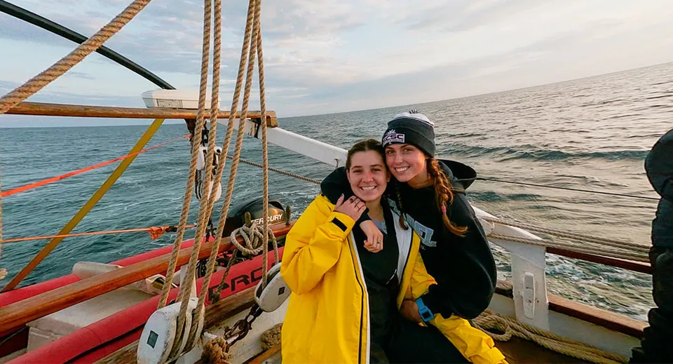 Due studentesse della Ashley Hall School si trovano sul ponte di una barca a vela con il mare aperto e un cielo nuvoloso sullo sfondo.