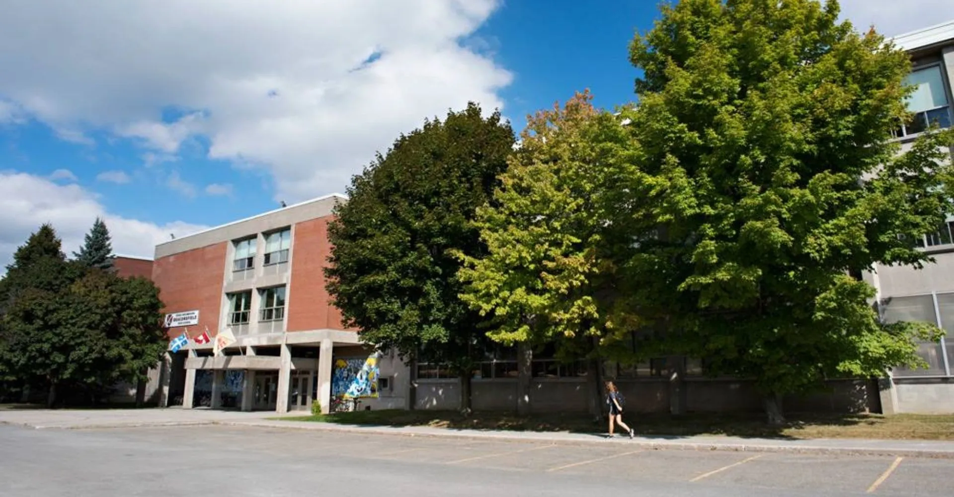 L'edificio a più piani della Beaconsfield High School si trova davanti ad alberi verdi sotto un cielo blu con nuvole.
