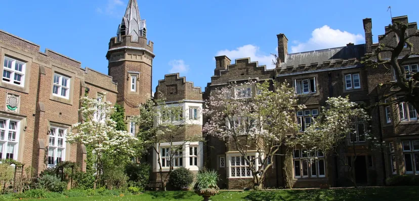 L'edificio storico in mattoni con un'alta torre si trova nel campus della Aldenham School, circondato da alberi verdi e piante in fiore.