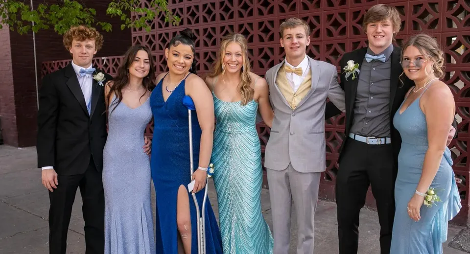 Un gruppo di persone ben vestite posa davanti a una struttura a griglia decorativa nel campus della Lord Tweedsmuir Secondary School.