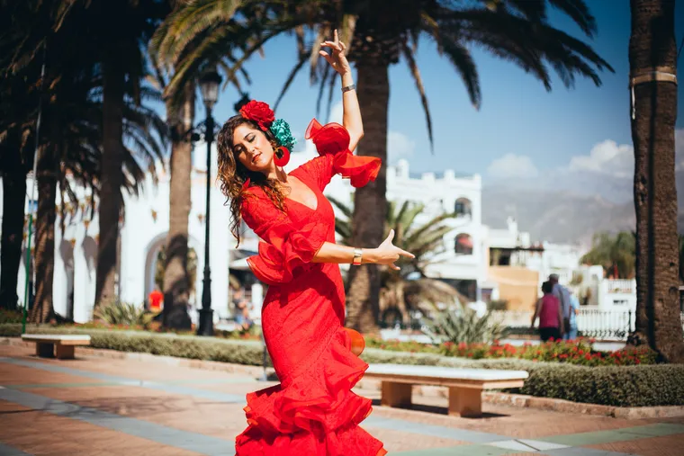 Flamencotänzerin im roten Rüschenkleid tanzt auf einer Promenade mit Palmen
