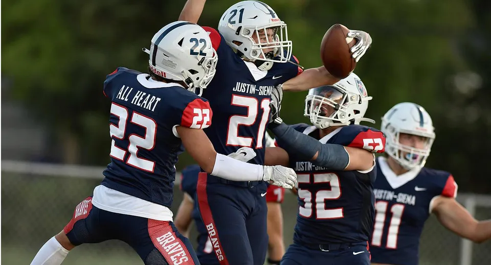 Un gruppo di giocatori di football della Justin Siena High School gioca su un campo d'erba sotto il cielo blu.