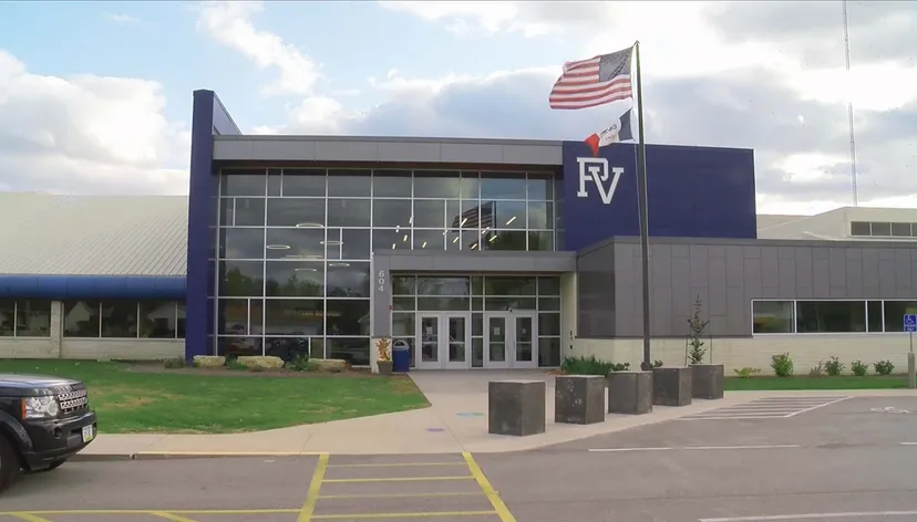 Il grande edificio blu e bianco della Pleasant Valley High School con la scritta RV e una bandiera americana all'esterno.