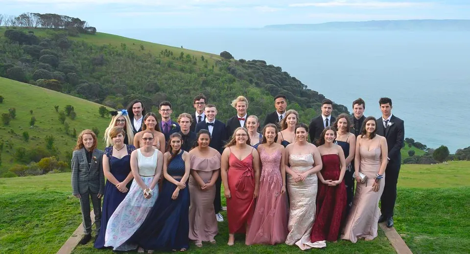 Un gruppo di persone in abiti formali si trova su un sentiero davanti a colline verdi all'interno del campus della Kangaroo Island Community Education.