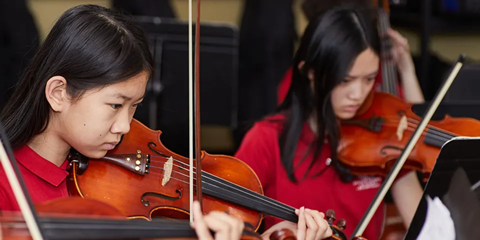 Due studentesse della Fulton Science Academy con polo rosse suonano il violino.